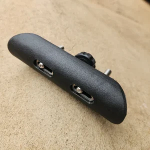 Three-quarter view of a black textured adjustable cheek pad showing top pad surface, adjustment slots, and mounting posts.