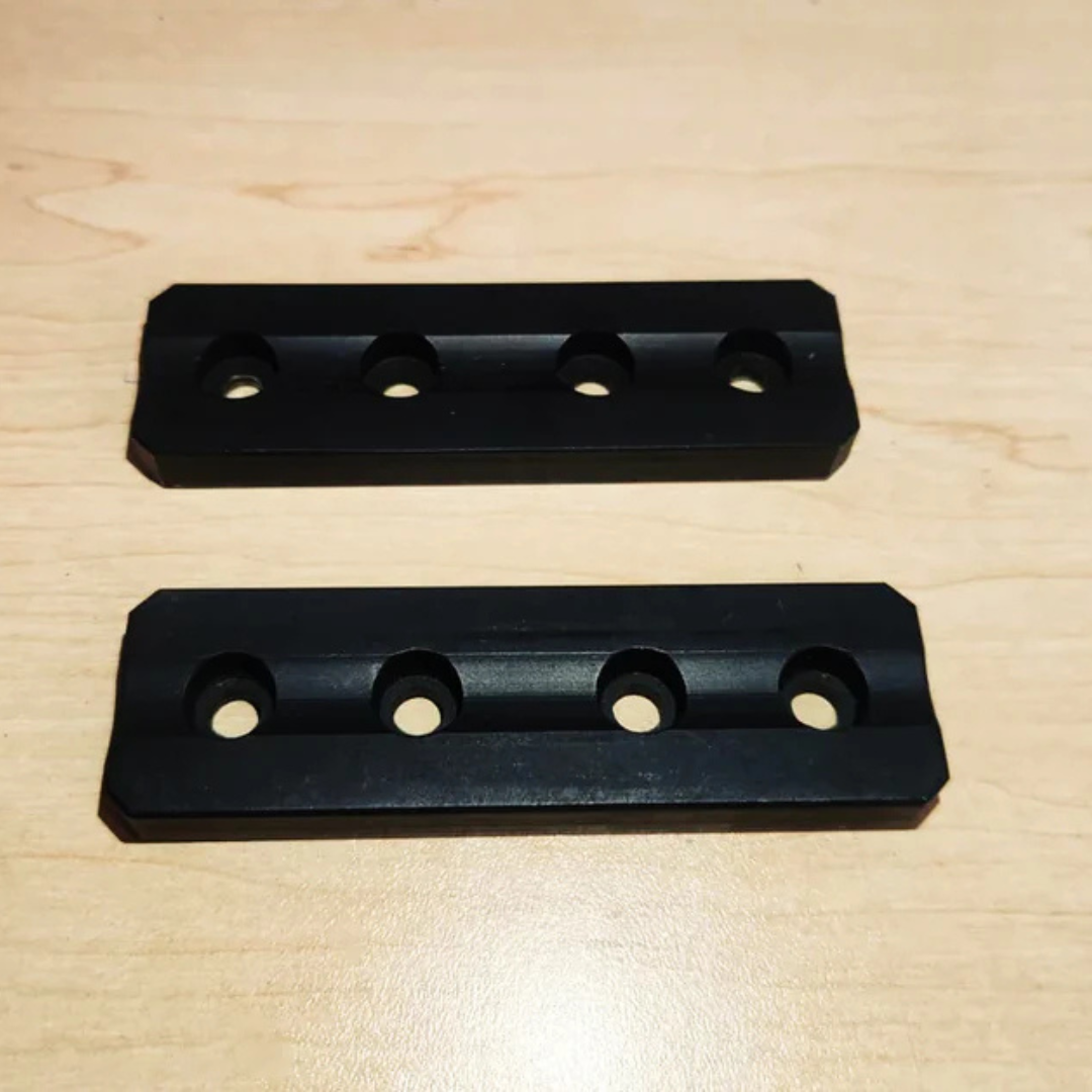 Overhead shot of two black loose weight blocks lying parallel on a wooden workbench.