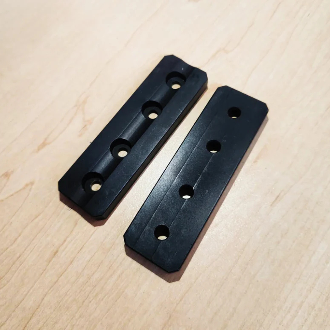 Two black chassis weight blocks showing counter-bored screw holes and bottom contact surface.